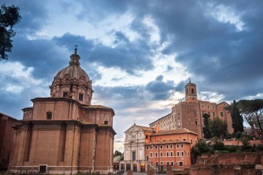 Roma Foro Romano 'nun kıyısındaki Santi Luca ve Martina' nın kubbeli kilisesine vuran gün batımı ışığı, Roma Foro Romano, İtalya 'nın Roma forumu, dramatik akşam bulutları gökyüzünde süzülürken.