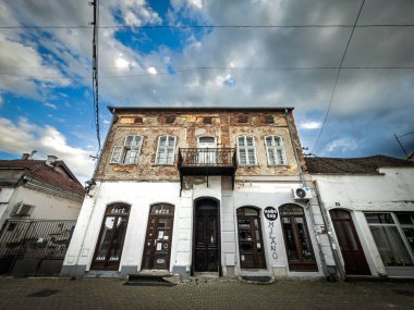 VALJEVO, SERBIA - 12 Mayıs 2025: şehir merkezindeki yıpranmış bir konak sokak seviyesinde küçük barlara ev sahipliği yapıyor. Korunmasız tuğla, soyulmuş alçı ve sarkık bir balkon kentsel bozulma ve ekonomik gerginliği gösteriyor..