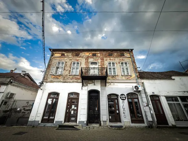 VALJEVO, SERBIA - 12 Mayıs 2025: şehir merkezindeki yıpranmış bir konak sokak seviyesinde küçük barlara ev sahipliği yapıyor. Korunmasız tuğla, soyulmuş alçı ve sarkık bir balkon kentsel bozulma ve ekonomik gerginliği gösteriyor..