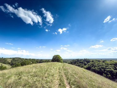 Voyvodina 'daki Zagajicka brda tepelerinde panoramik manzara. Yeşil tepeler, çayırlar ve uzak ormanlar dağınık bulutlu mavi gökyüzünün altında geniş bir ufuk oluşturur..