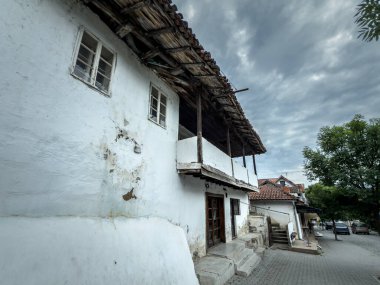 Sırbistan 'da beyazlatılmış duvarları, kereste balkonu ve fayanslı çatısı olan geleneksel Balkan evi. Yıpranmış alçı ve taş basamaklar bulutlu bir gökyüzünün altında dar bir köy caddesi boyunca yaşlılık ve çürüme gösteriyor..