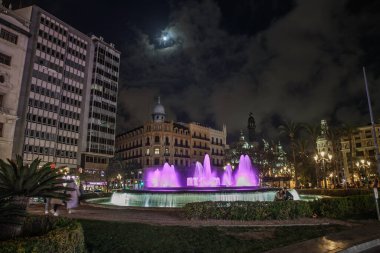 VALENCIA, İspanya - 15 Nisan 2025: Valencia, İspanya 'da Placa de l' Ajuntament 'in gece panoraması, tarihi binalar ve şehir ışıklarıyla çevrili tarihi mehtaplı gökyüzü altında.