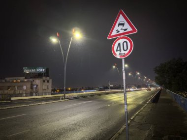 BELGRAD, SERBIA - 22 Nisan 2025: Kentsel sürüş koşullarını gösteren ıslak bir yolda hız sınırı ve kaygan yol uyarısıyla Belgrad 'daki Brankov Most köprüsünün gece görüntüsü.
