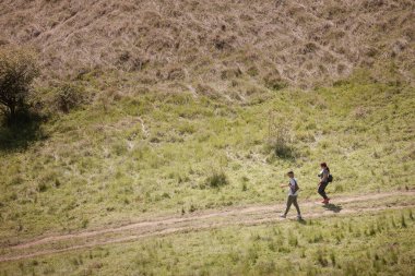 DELIBLATO, SERBIA - 1 Mayıs 2025: Sırbistan 'ın Voyvodina kentindeki Zagajicka brda tepelerinde iki yürüyüşçü çimenli bir yoldan iniyor. Günübirlik yürüyüşlerde hafif sırt çantaları ve günlük kıyafetlerle..