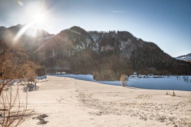 Slovenya 'nın Zgornje Jezersko şehrinde Julian Alpleri' nde geniş karlı bir ova. Kış güneşi uzun gölgeler bırakır ve beyaz çayırlarda izler bırakır. Ufukta ağaçlık yamaçlar ve dağınık çiftlikler vardır.