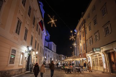 LJUBLJANA, SLOVENIA - 17 Aralık 2024: Ljubljana şehir merkezindeki Ciril Metodov 'un akşam manzarası. Sakin bir kış gecesinde tarihi cepheler arasında kar tanesi ışıkları yayılır..