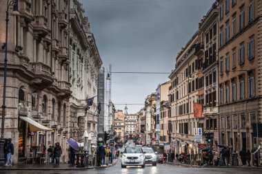 Roma, İtalya - 19 Ocak 2025: Eski Roma, İtalya 'da arabaların ve yayaların tarihi binaların yanından geçtiği merkez caddede yağmurlu bir gün trafiği. Islak asfalt çerçevesi Eski şehrin perspektifi.