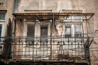 Belgrad 'da kötüye giden bir konut binasında terk edilmiş bir balkon. Çatlak alçı, paslı korkuluklar ve kıvrımlı bir tepe örtüsü eski apartman cephesinde kentsel bozulmayı ve bakımsızlığı gösteriyor..