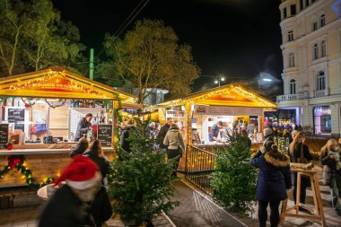 GRAZ, AUSTRIA - 21 Aralık 2024: Işıklı ahşap tezgahlar, Graz, Avusturya 'daki Advent pazarı olan Graz Adventmarkt' ta, bayram sezonu için ana noel pazarında yiyecek ve içecekler servis etmektedir..