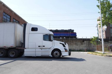 Kamyon, tren ve klasik binalarla güneşli bir gün sahnesi