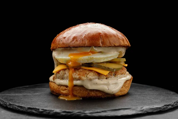 Burger with chicken patty, egg and cheese, on a black background