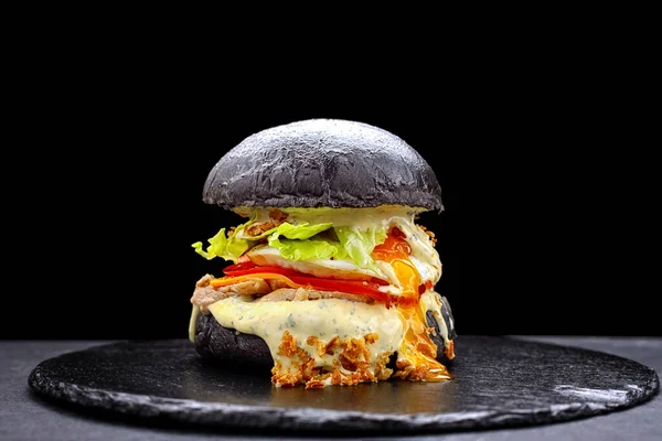 Cuttlefish ink burger with chicken, egg and vegetables, on a black background