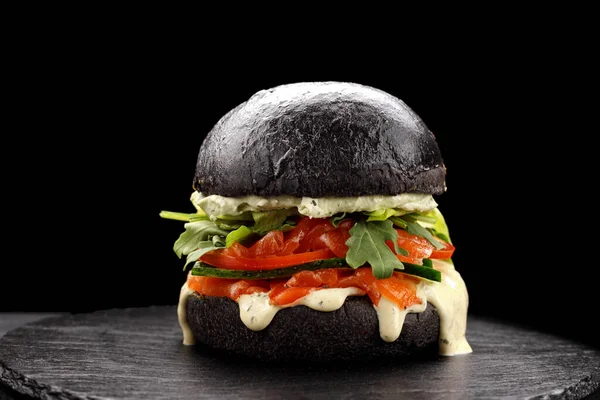Cuttlefish ink burger with salmon, egg, herbs and vegetables, on a black background