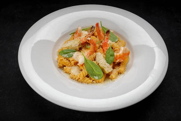 Pasta with shrimps, cheese and spices on a plate, on dark concrete