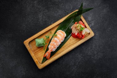 Nigiri Ebi ahşap bir tahtanın üzerinde wasabi ve zencefil ile, karanlık bir arka planda.