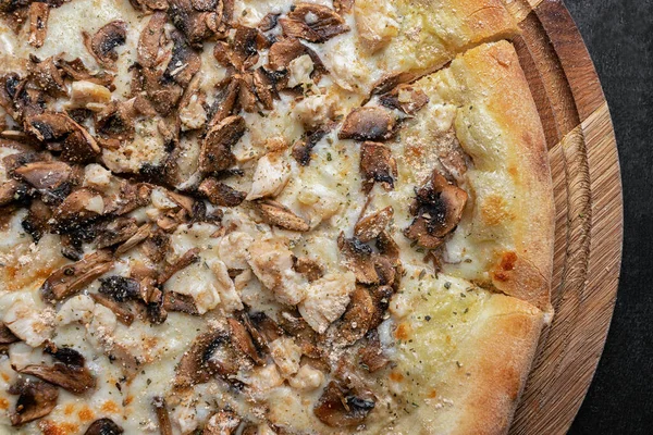 Pizza with mushrooms, chicken and cheese on a wooden board
