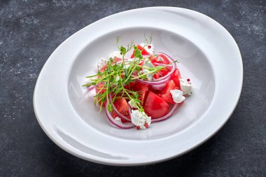 Bir tabakta domatesli salata, bitki ve peynir.