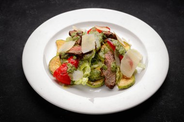 Dana eti, kızarmış sebze ve koyu arkaplanda parmesan peynirli salata.