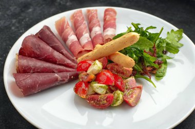 Peynirli salata, domates ve somon, tabakta, koyu betonda.