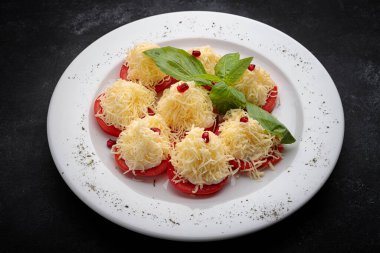 Peynirli ve mayonezli dilimlenmiş domatesler. Koyu bir arka planda.