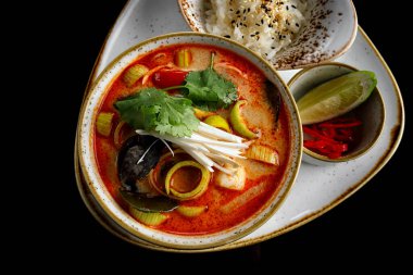 Tom Yum çorbası, karides, midye ve mürekkep balığı, siyah arka planda.