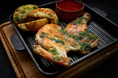 Kızarmış yarım tavuk, kızarmış patates ve baharatlı sos. Kızartma tavasında, tahta tahtada ve koyu arka planda.