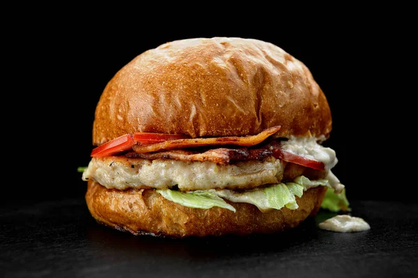 Burger with chicken patty, bacon and tomatoes, on a dark background