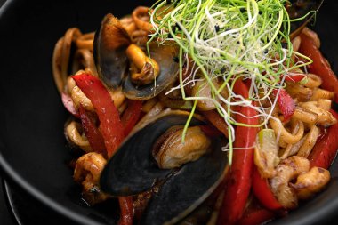 Siyah bir tabakta deniz ürünleri ve sebzeli makarna, ahşap bir arka planda, bulanık bir arka planda