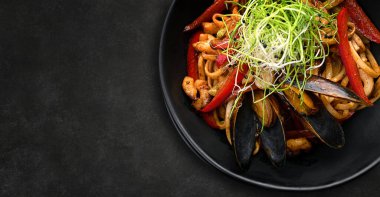 Siyah bir tabakta deniz ürünleri ve sebzeli makarna, ahşap bir arka planda, bulanık bir arka planda