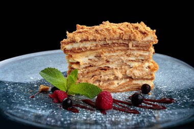 Bir parça Napolyon pastası, böğürtlenli ve naneli, siyah arka planda.