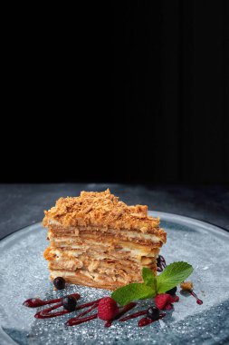 Bir parça Napolyon pastası, böğürtlenli ve naneli, siyah arka planda.