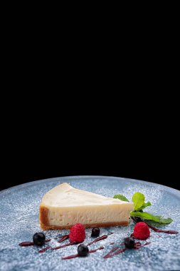 Siyah arka planda böğürtlen ve nane aromalı bir cheesecake.