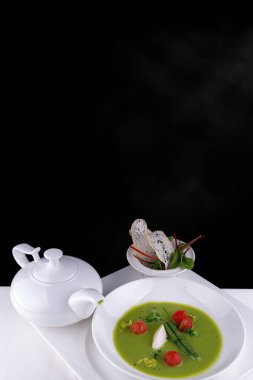 Yeşil bezelye çorbası, domates ve kızarmış ekmek, beyaz arka planda.