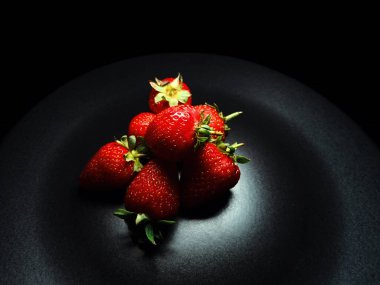 Siyah arka planda, siyah bir tabakta olgun çilekler. Stüdyo ışığı