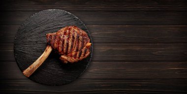 Tomahawk bifteği siyah bir tahtada, ahşap bir arka planda