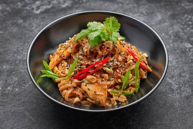 Tavuklu ve sebzeli erişte, siyah bir tabakta, arka planda.