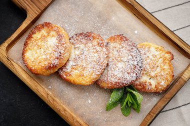 Tahta tahtada pudra şekerli peynirli kekler, koyu arkaplanda.