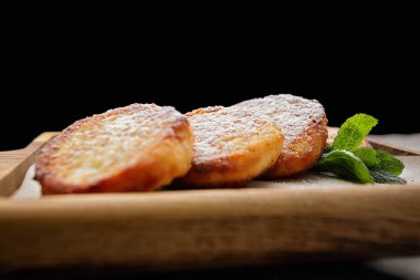 Tahta tahtada pudra şekerli peynirli kekler, koyu arkaplanda.