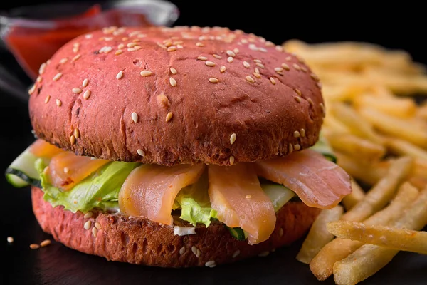 Red burger with salmon, lettuce and cucumber, with potatoes and sauce on a blurred background