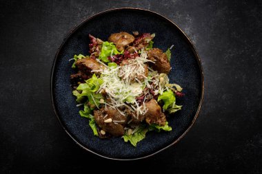 Warm salad with liver, cheese and lettuce, on a dark background
