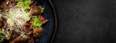 Warm salad with liver, cheese and lettuce, on a dark background