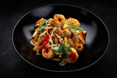 Pasta with shrimp and vegetables, Asian food. black plate, on gray concrete