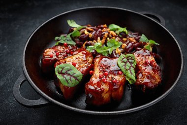 Grilled ribs in a sauce with beans, in a pan, on gray concrete