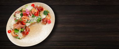 Salad with shrimp, prosciutto and cheese on a plate, on a wooden background. Banner