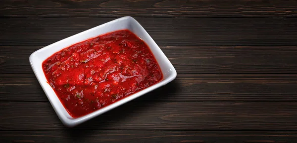 Spicy tomato sauce with herbs, in a white sauce pan, on a wooden background