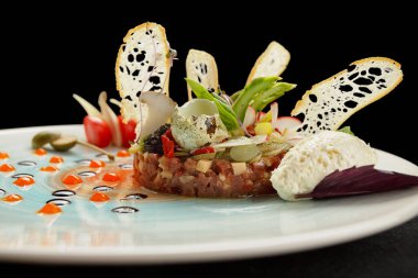Salmon tartar with quail egg and bread chips, on a black background