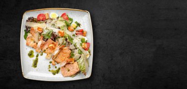 Caesar salad with shrimp and trout, in a plate, on a dark concrete background. Banner