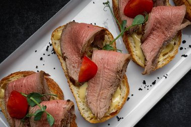 Bruschetta with meat, sauce and tomatoes, on a dark background