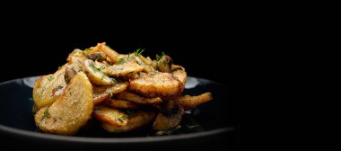 fried potatoes with mushrooms and dill in a dark plate, on a black background