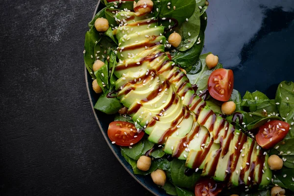 salad with avocado, nuts, tomatoes and sauce. on a dark background